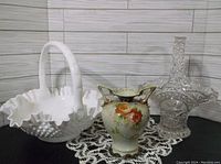 White hobnail Fenton glass basket, Hoffbauer crystal basket, and floral porcelain vase arranged on lace doily