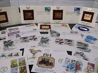 Full overview of envelopes with stamps and gold-tone Olympic plaques in white mounts spread out on table.