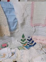 Various vintage linens including crocheted doilies, embroidered cloths, and table runners spread out, showing different textures, colors, and designs.