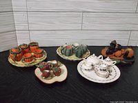 Five miniature tea sets: four with pumpkin designs in resin, one white porcelain set with floral decoration on a separate tray.
