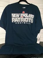 Front view of navy blue T-shirt displaying large 'New England Patriots Football' logo graphic in white and red.