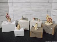 Six Sebastian Miniatures displayed on cardboard boxes against wood panel background. Includes small buildings, figurines, and dioramas.