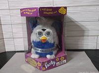 Furby in original purple box, white and blue fur with plastic eyes and beak, text on box indicates Special Millennium Edition