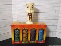 Ceramic tiki mug in Fu Man Chu style on top of the boxed set of four tiki mugs, showcasing the packaging and one mug's design.