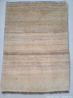 Top view of entire rug showing beige and light brown horizontal stripes pattern, thick plush wool pile, and fringed edges.