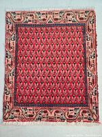 Full view of the front side of the wool Persian Mir rug showing red field with paisley motifs and beige geometric border with fringe ends.
