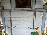 Two large metal anchors hanging on a painted wooden wall, both with attached long rusted chains.