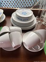 Photo of stacked small plates, saucers, and coffee cups showing the blue cornflower pattern and white ceramic finish.