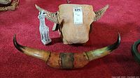 Front view of woven cow head, pair of long cow horns, and carved animal figurine showing details and relative sizes.