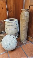 View of all three items: the pottery crock, tall pottery vase, and stone ball on tiled floor.