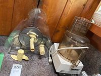 White Cuisinart food processor base with attached clear plastic bowl, power cord visible, beige plastic blades and attachments in front.