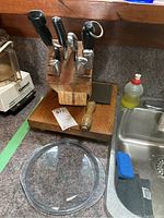 Wooden knife block with knives and solid steel cleaver on wooden base, glass baking dish with lid beside the sink.