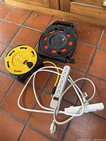 Photo showing four extension cords/power strips including two reel-style outdoor extension cords and two indoor power strips.