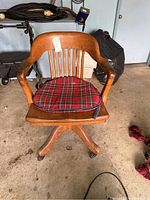 Front view of wooden swivel office chair with plaid cushion showing seat, armrest, and wheel base.