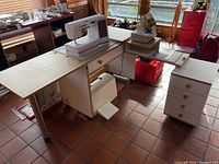 Wide photo showing sewing table setup with sewing machine on metal platform, separate drawer cabinet beside it, and additional drawer under the table.