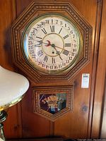 Front view of vintage wall clock with wooden octagonal frame hung on a wall near a lamp, showing full clock face and lower window with 'STANDARD TIME' lettering.