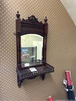 Front and angled views of vintage wooden wall mirror showing carved details, shelf, and mirrored glass with wear.