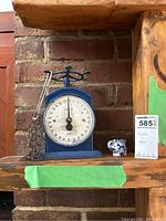 Photo showing the blue vintage Salter kitchen scale and Indian elephant toothpick holder on a wooden shelf with a brick background.