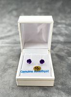 Pair of 10kt white gold stud earrings with purple amethyst stones displayed in an open white jewelry box with '10kt Genuine Amethyst' label visible.