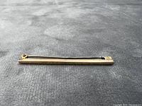 Side view of the antique 10kt gold pin laid flat on a textured grey surface, showing its thin rectangular shape.