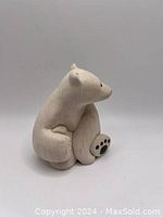 White polar bear figurine sitting with front foot showing black paw prints, side view.