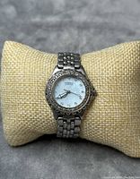 Fossil ladies quartz watch with mother of pearl dial and rhinestones on bracelet cushion, showing overall appearance and metal link bracelet.