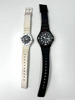Top view of two Casio diver style watches side by side on white background. One is black men's MRW-200 and one is white women's LRW-200H.