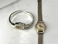 Two Swiss-made ladies mechanical watches, one with mesh band (Everite) and one cuff-style band (Anker), silver-tone cases, on a white surface.