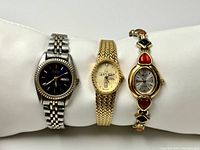 Photo showing three ladies quartz watches on white display pillow: Embassy by Gruen with black dial and stainless steel band; Sarah Coventry gold-tone watch with mesh band; Kathie Lee gold-tone watch with decorative heart and diamond bracelet