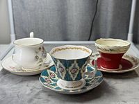 Front view of three teacup and saucer sets showing detailed designs and colors.