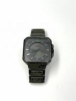 Front view of Nixon watch with black square case and black metal bracelet on white background.