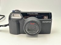 Front view of Olympus Superzoom 2800 film camera showing lens, built-in flash, and button layout.