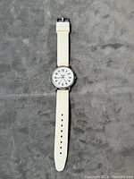Full view of white strap quartz watch with round face on grey background