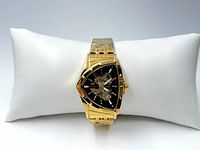 Front view of gold-tone triangle-shaped men's wristwatch on white pillow showing skeleton dial and gold bracelet.