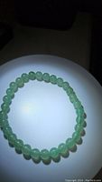 Front-facing photo of a circular bracelet made from round green aventurine beads on a white surface under bright light.