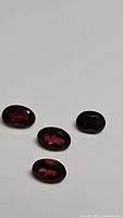 Four oval faceted cherry red almandine garnet gemstones on a white background showing cut and color.