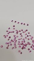 Image showing multiple tiny round diamond cut pink sapphire gemstones spread on plain background, highlighting their bubblegum pink color and clarity.