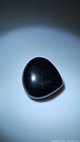 Glossy black onyx teardrop cabochon gemstone showing surface and shape details.