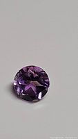 Close-up front view of round faceted purple amethyst gemstone showing diamond cut facets and clarity.