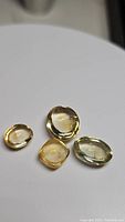 Four golden citrine cabochons of different shapes and sizes placed on a white surface. Visible inclusions inside the stones can be observed.