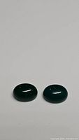 Two polished oval cabochon green onyx gemstones on neutral background, shown in natural lighting.