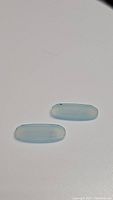 Top view of two elongated oval icy blue chalcedony gemstones on a white background, showing color and shape.
