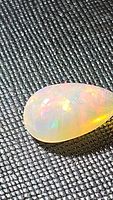 Close-up image showing the teardrop-shaped Ethiopian opal with rainbow play of color on a textured black background.