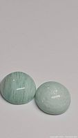 Pair of round polished amazonite stones showing ribins egg blue colors with natural patterning under clear lighting on plain background.