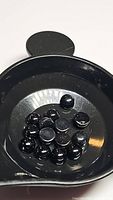 Photo of multiple small black round cabochon gemstones in a black measuring tray.