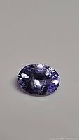 Close-up image of the natural bright blue-purple oval cut tanzanite gemstone showing facets and internal clarity.