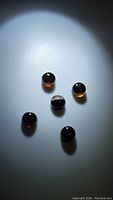 Five natural chocolate brown onyx round polished gemstones under spotlight on a neutral surface.