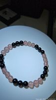 Image showing natural black onyx and rose quartz beads bracelet on a white display surface. The bracelet is circular and the beads are smooth and polished.