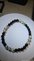 Stretchy natural gemstone bracelet composed of polished black onyx beads and cream dalmatian jasper beads with black spots, displayed flat on a white circular surface.