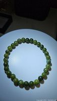 Close-up image of natural green jade bead bracelet arranged in a circular shape on a plain background.